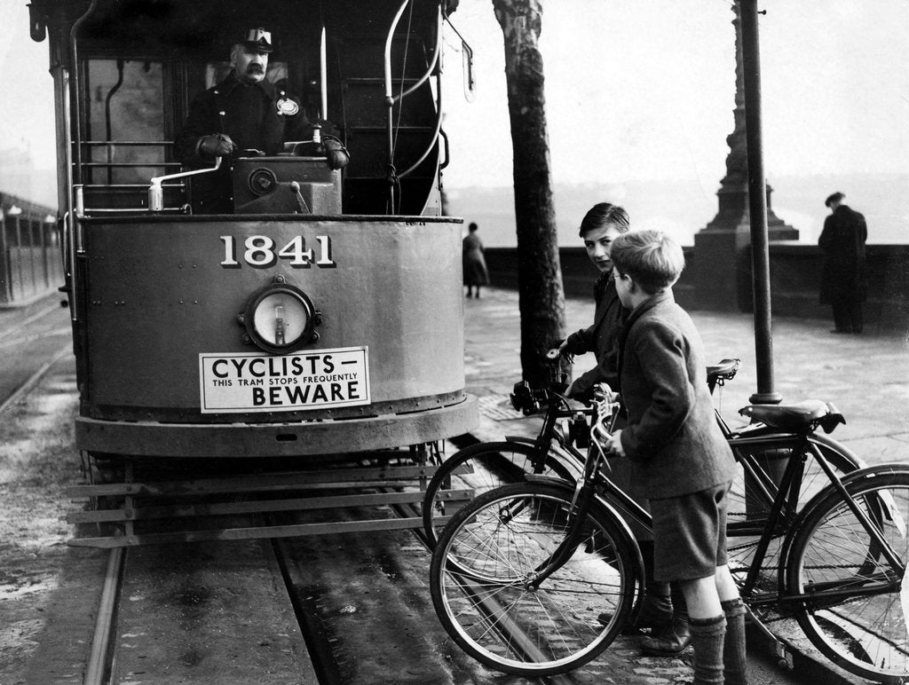 Detail of Boys on bicycles cross in front of a tram by Associated Newspapers