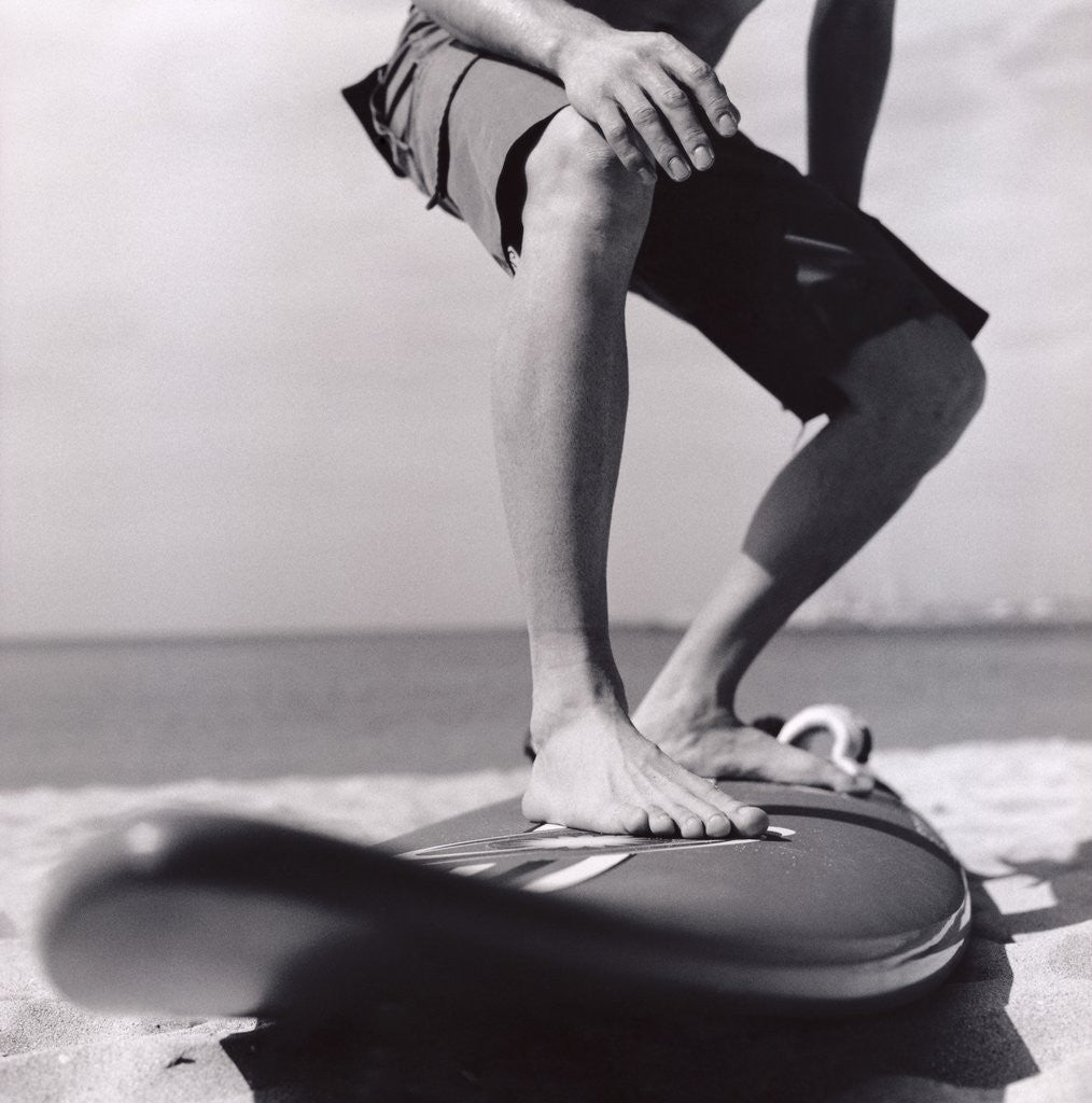 Detail of Young Man Standing on Surfboard on the Beach by Corbis