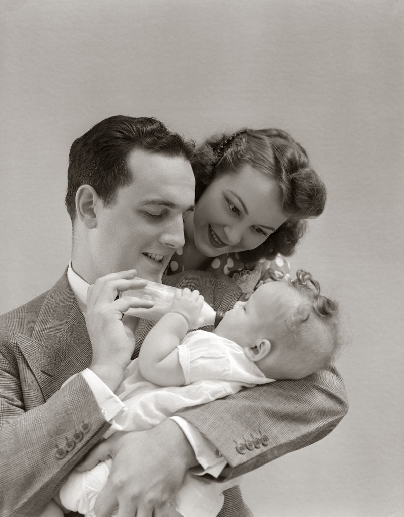 Detail of 1940s Father Cradling Baby Daughter Feeding Her Bottle With Mother Looking Over His Shoulder by Anonymous