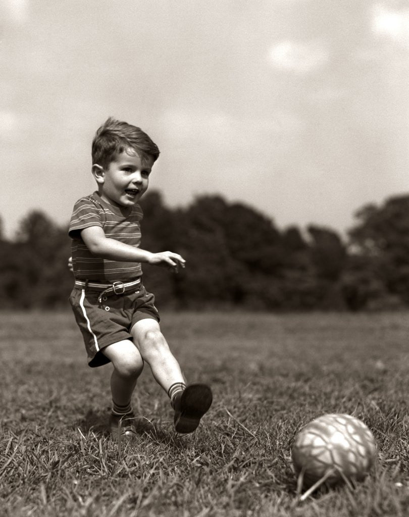 Detail of 1940s Boy Kicking Ball In Grassy Field by Corbis