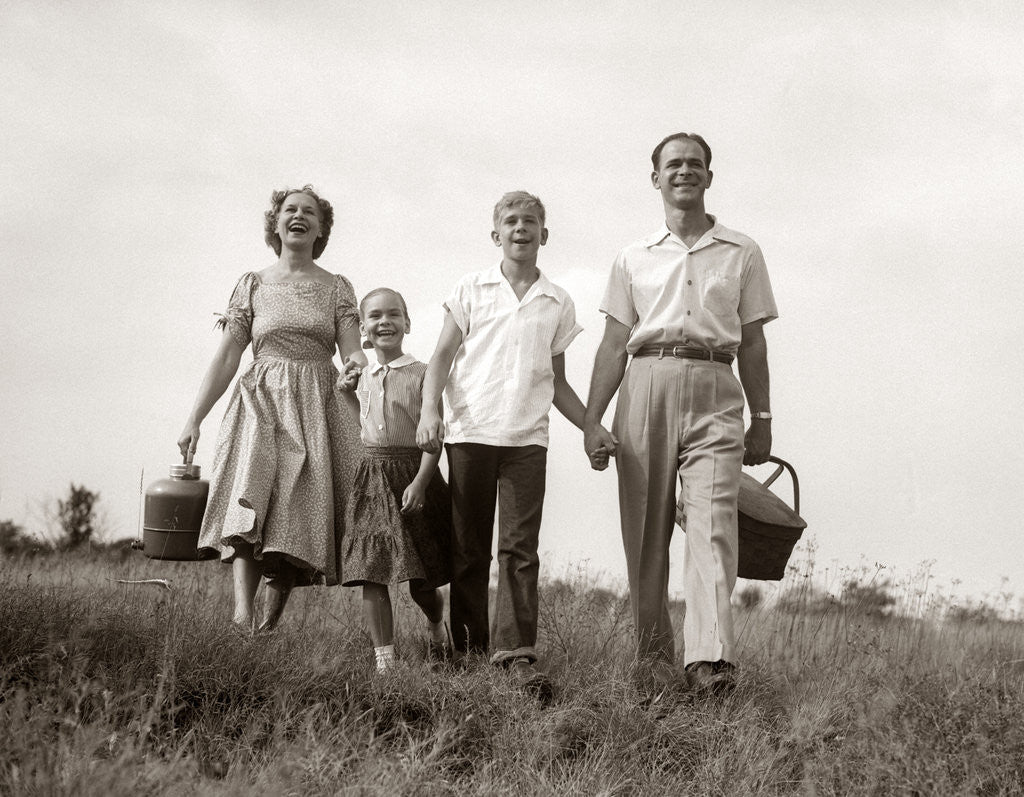 Detail of 1950s Family Walking In Grassy Meadow Carrying Summer Picnic Basket And Thermos by Corbis