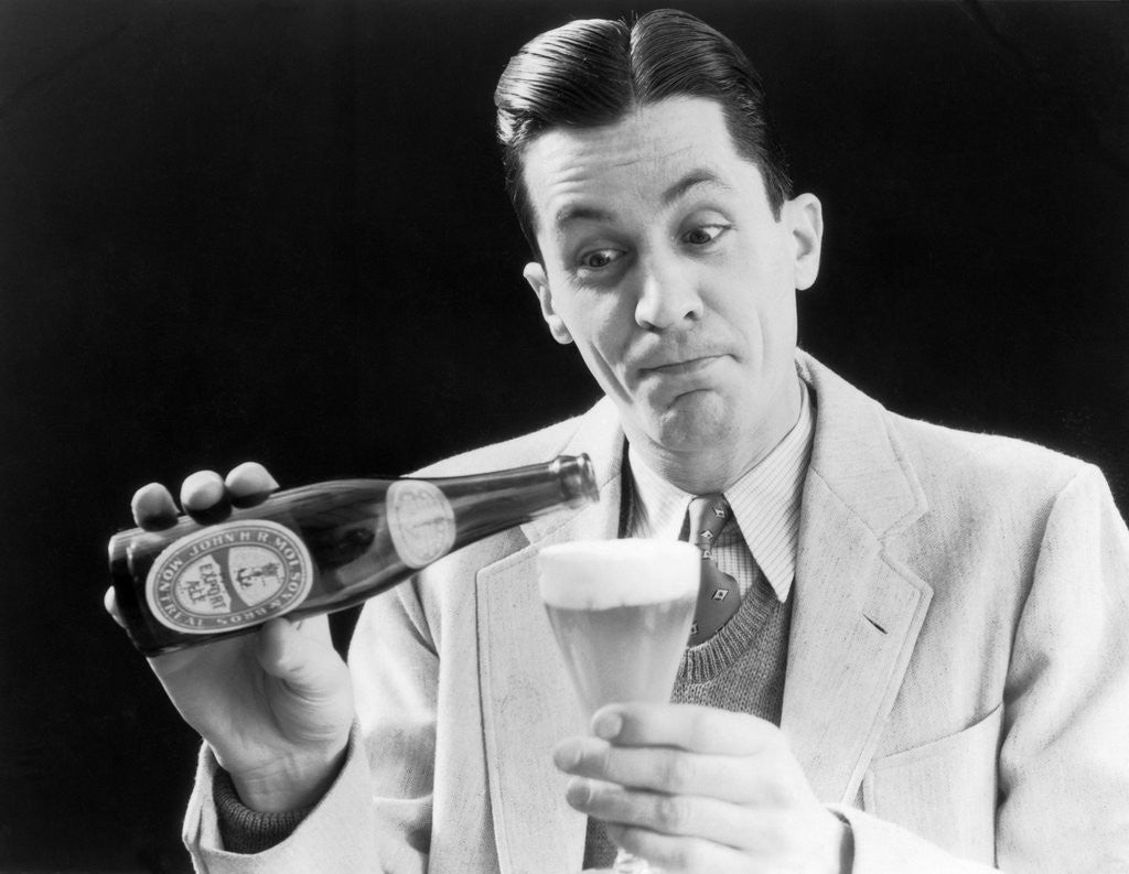 Detail of 1930s Man Pouring Beer From Bottle Into Glass Look Of Anticipation Wearing Suit Tie Sweater by Corbis