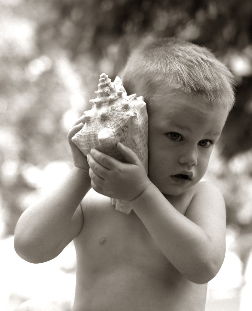 Detail of 1960s Boy Toddler Holding Seashell To Ear Listening To Ocean Sounds Summer Beach by Anonymous