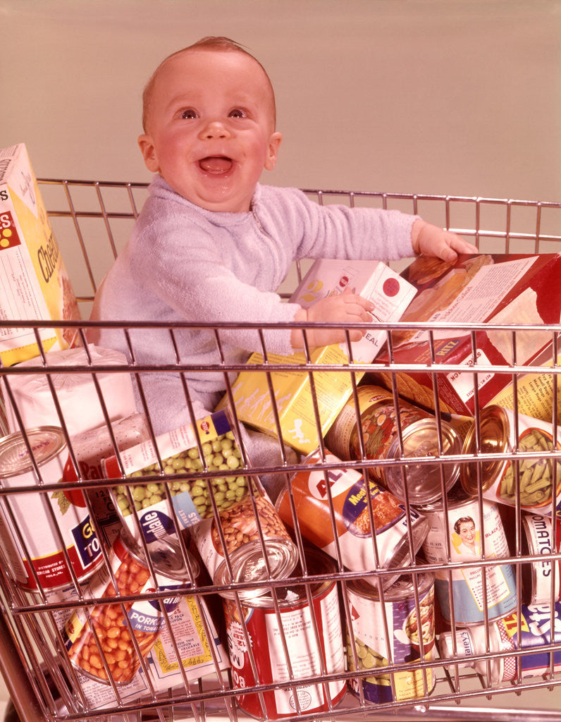 Detail of 1960s Happy Baby Sitting Inside Shopping Cart Full Of Groceries by Corbis