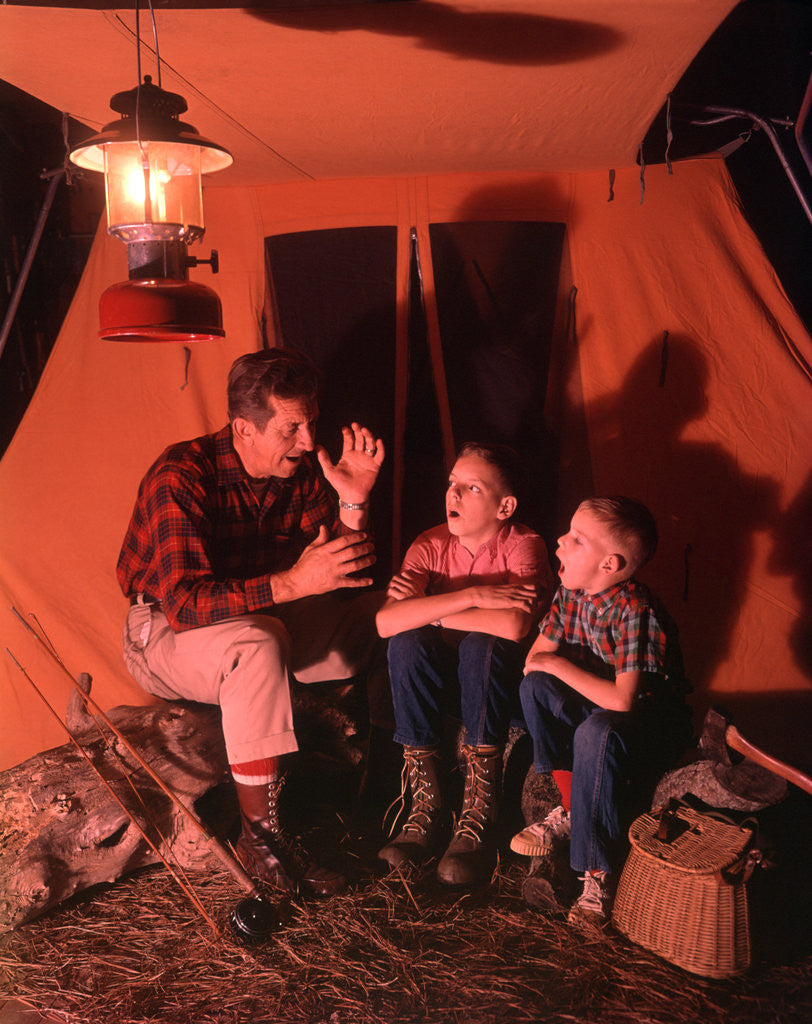 Detail of 1960s 1970s Grandfather Telling Scary Story To Boys By Tent At Night Campsite In Shadows by Anonymous