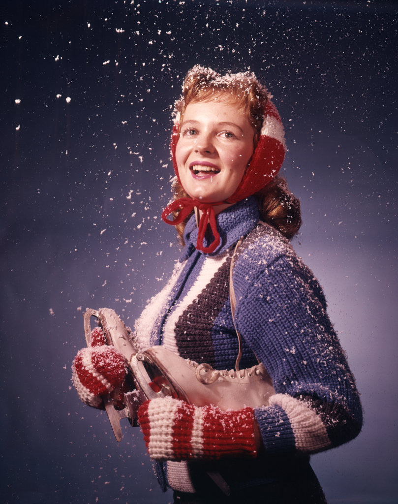 Detail of 1960s Young Woman Wearing Red Mittens Ear Muffs Blue Sweater Holding Ice Skates In Falling Snow by Anonymous