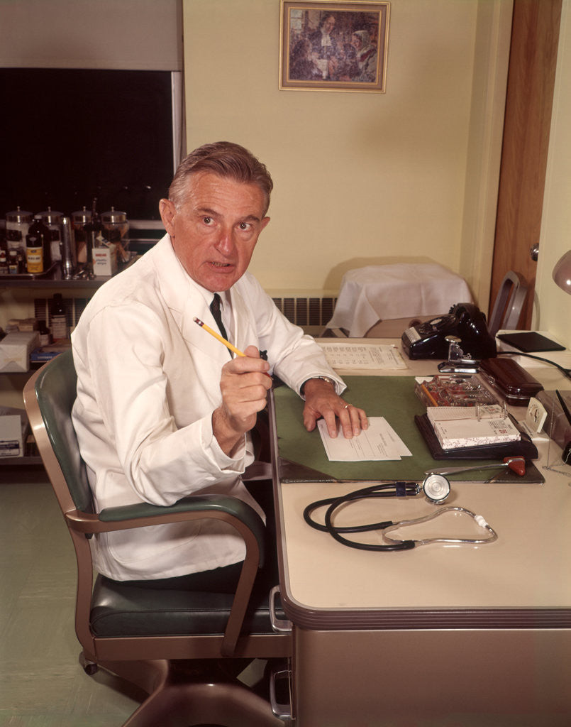 Detail of 1960s Man Doctor Pointing Gesturing With Pencil Seated At Desk In Office by Corbis