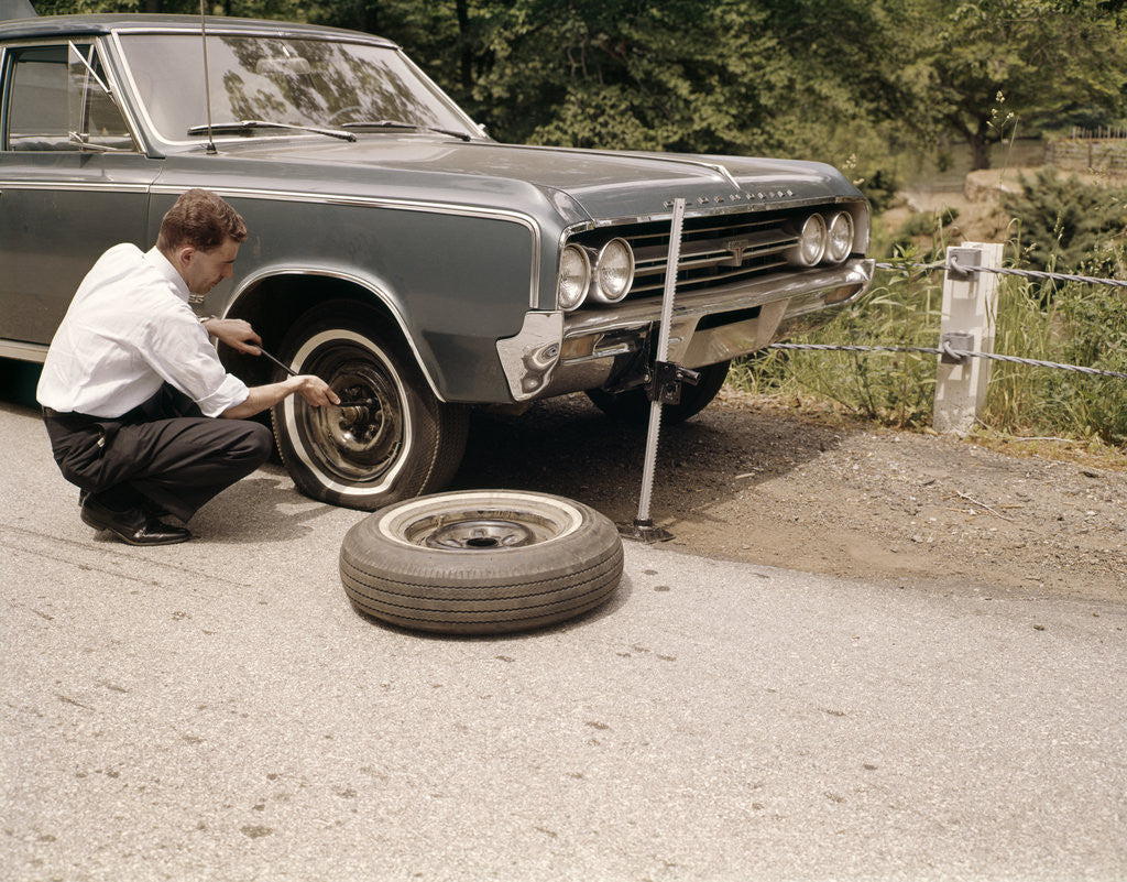Detail of 1960s Man Changing Flat Tire On Car At Side Of Rural Road Car Jack Tools Tire Iron by Anonymous