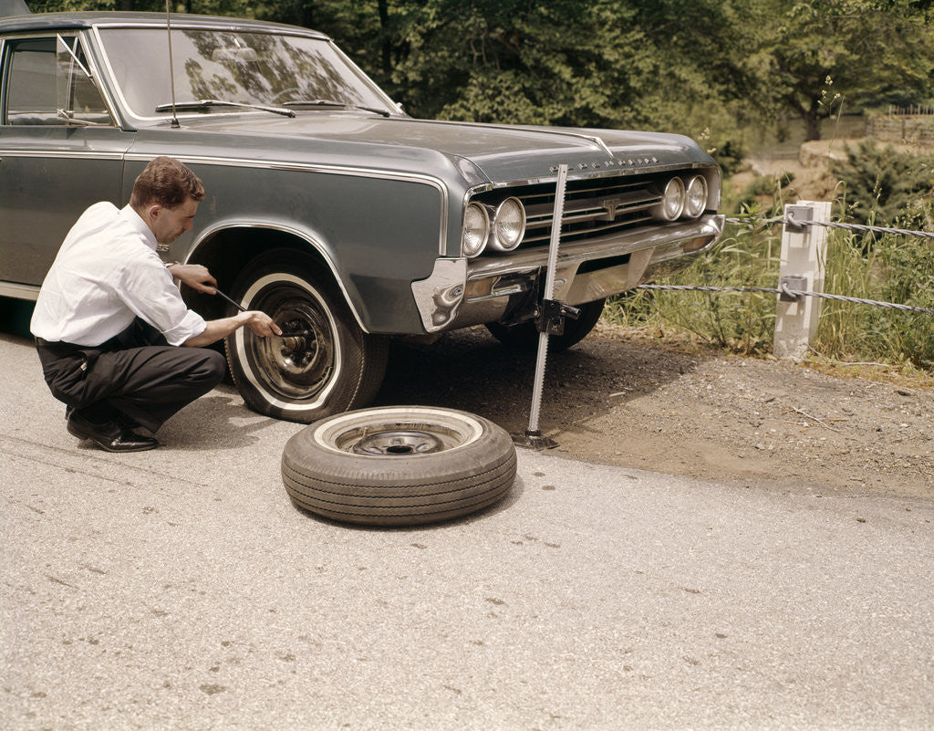 Detail of 1960s Man Changing Flat Tire On Car At Side Of Rural Road Car Jack Tools Tire Iron by Corbis