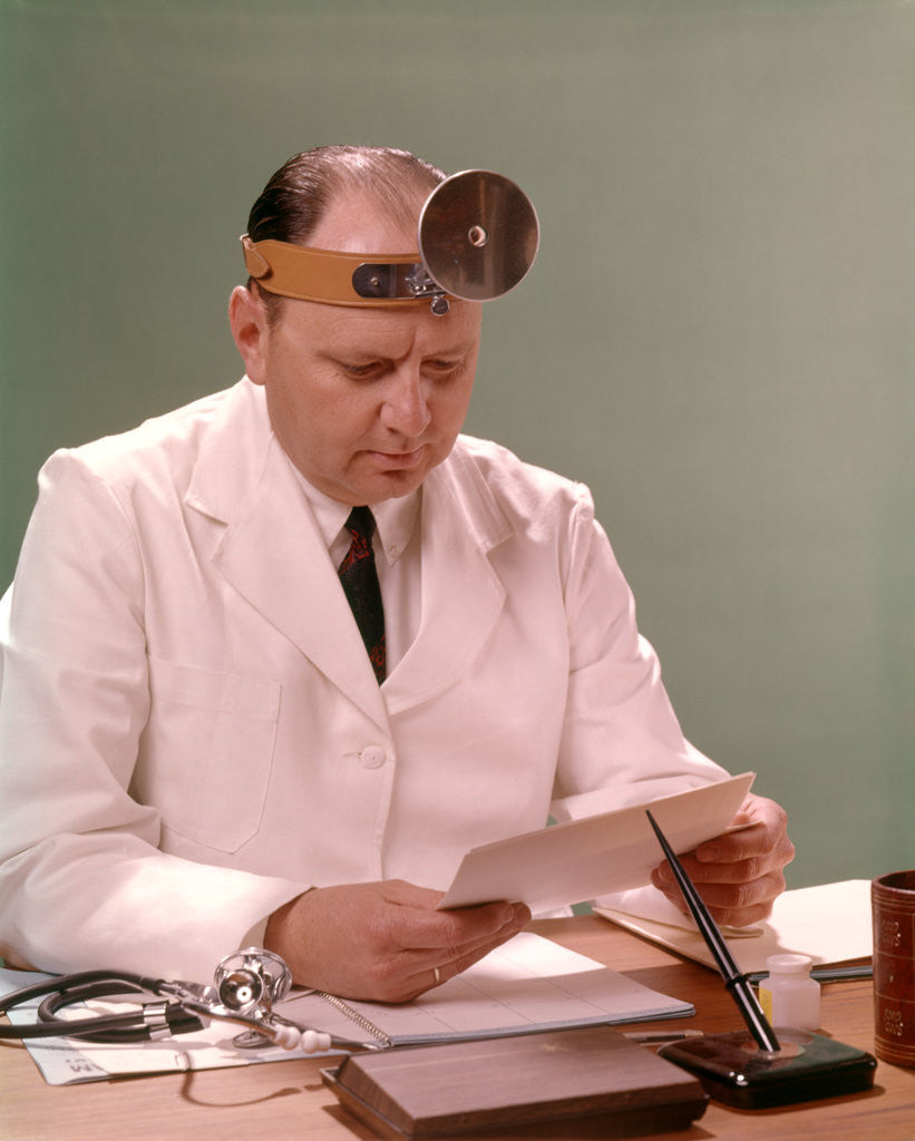 Detail of 1960s Man Doctor Seated At Desk Reading Paperwork by Anonymous