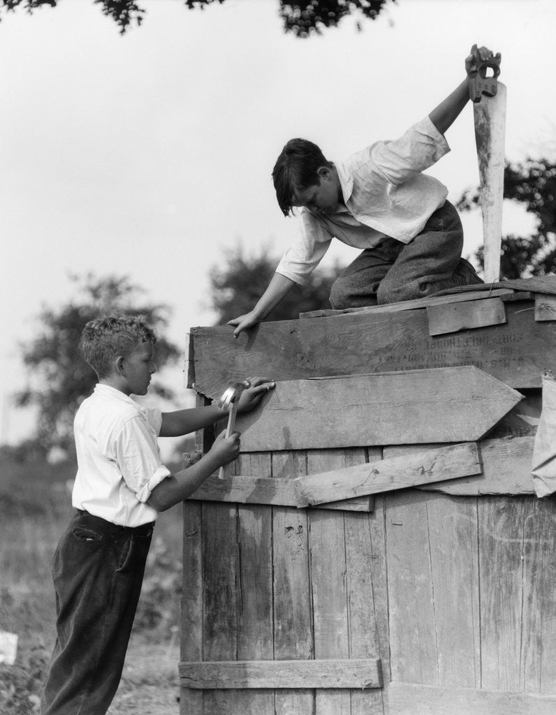 Detail of 1930s Pair Of Boys Building Shack One Nailing Board To Side One On Roof With Saw by Anonymous