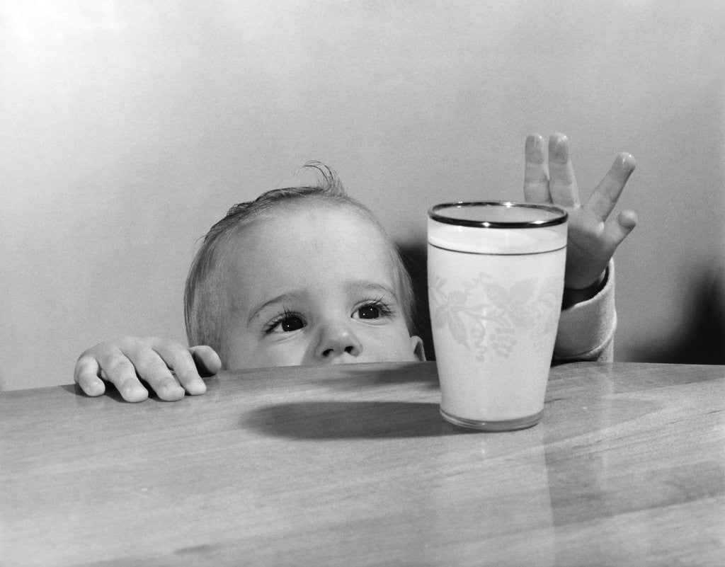 Detail of 1950s Toddler Reaching Up To Table To Grab Milk Glass by Anonymous