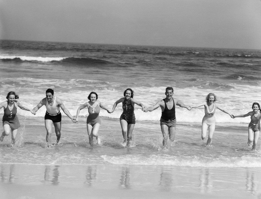 Detail of 1930s Group 7 People Holding Hands Running Out Of Surf Onto Beach by Corbis
