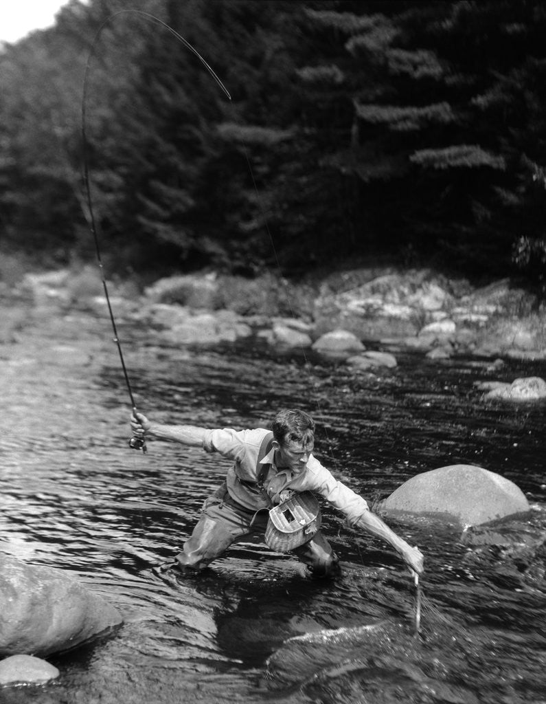 Detail of 1920s Man In Stream Wearing Waders With Fish On Line Trying To Catch It In Net by Corbis