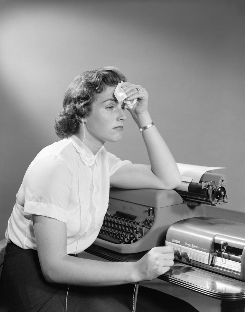 Detail of 1950s Ailing Secretary Sitting At Desk With Typewriter And Dictation Machine Holding Handkerchief To Forehead by Anonymous
