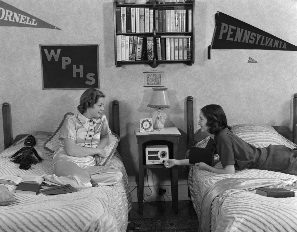 Detail of 1930s 1940s Two Teen Girls Lying On Dormitory Beds Room Mates Listening To Radio College School Pennants On Wall by Anonymous