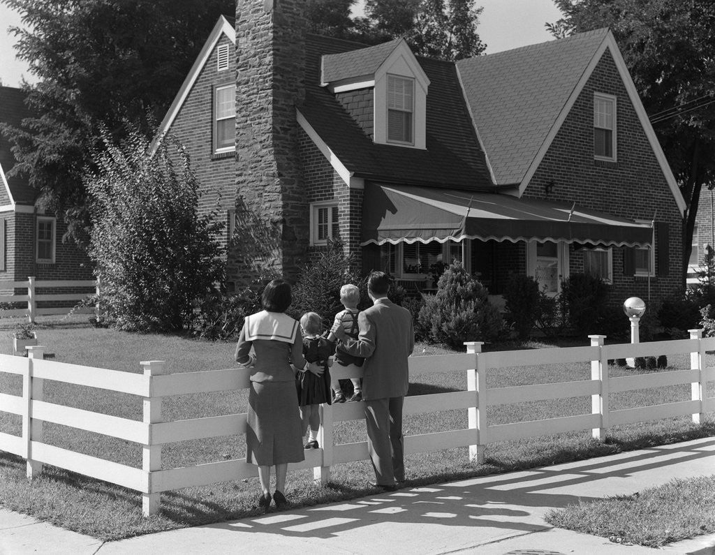 Detail of 1950s Family Standing By White Fence Looking At Brick House by Anonymous