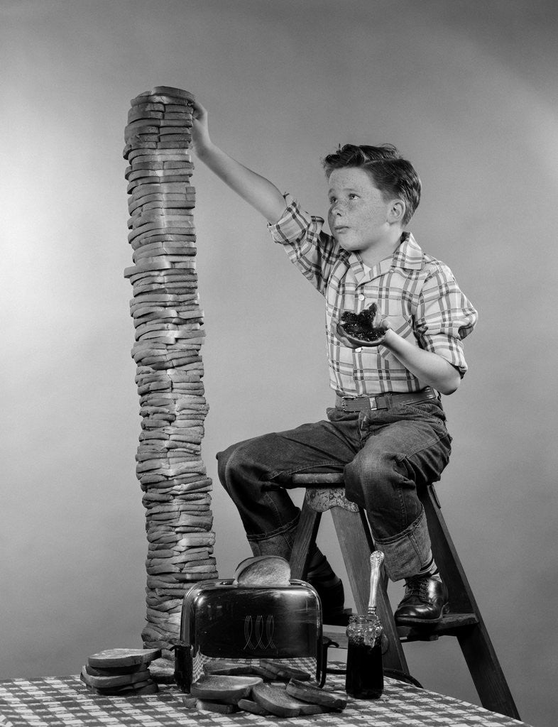 Detail of 1950s Boy Eating Jelly Toast Sitting On Ladder Stacking Up Tall Pile Of Toast From Toaster by Corbis