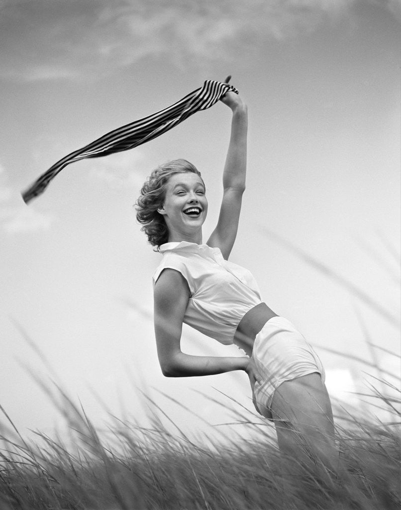 Detail of 1950s 1960s Young Woman Bending Back Holding Scarf In The Wind Standing On Grassy Beach Dune by Anonymous