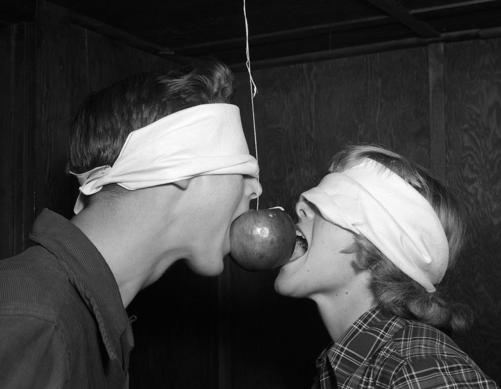 Detail of 1950s Blindfolded Couple Trying To Eat An Apple Hanging In Air From A String Inside by Corbis