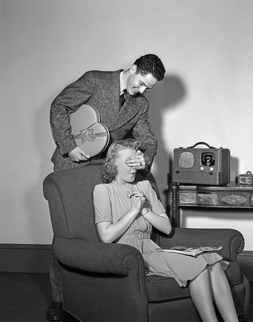 Detail of 1940s Teen Couple Boy With Hand Over Girl Eyes Surprising Her With Box Of Valentines Day Candy by Corbis
