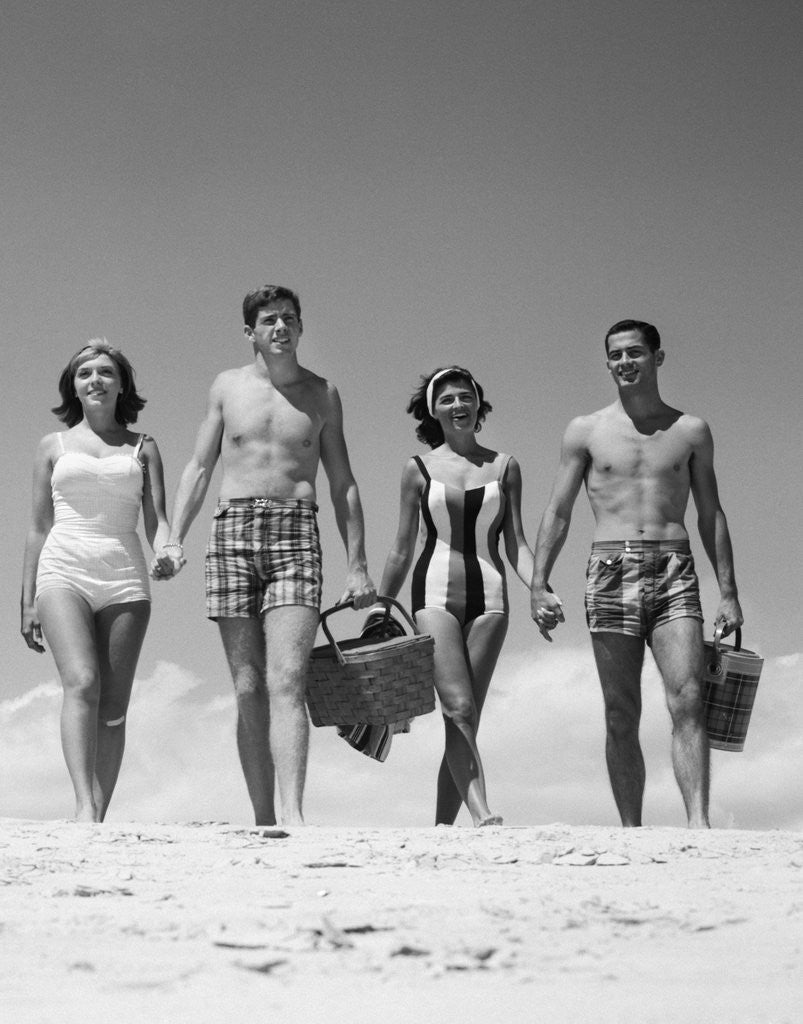 Detail of 1960s Teenage Couples Wearing Bathing Suits On Beach Carrying Picnic Baskets by Anonymous
