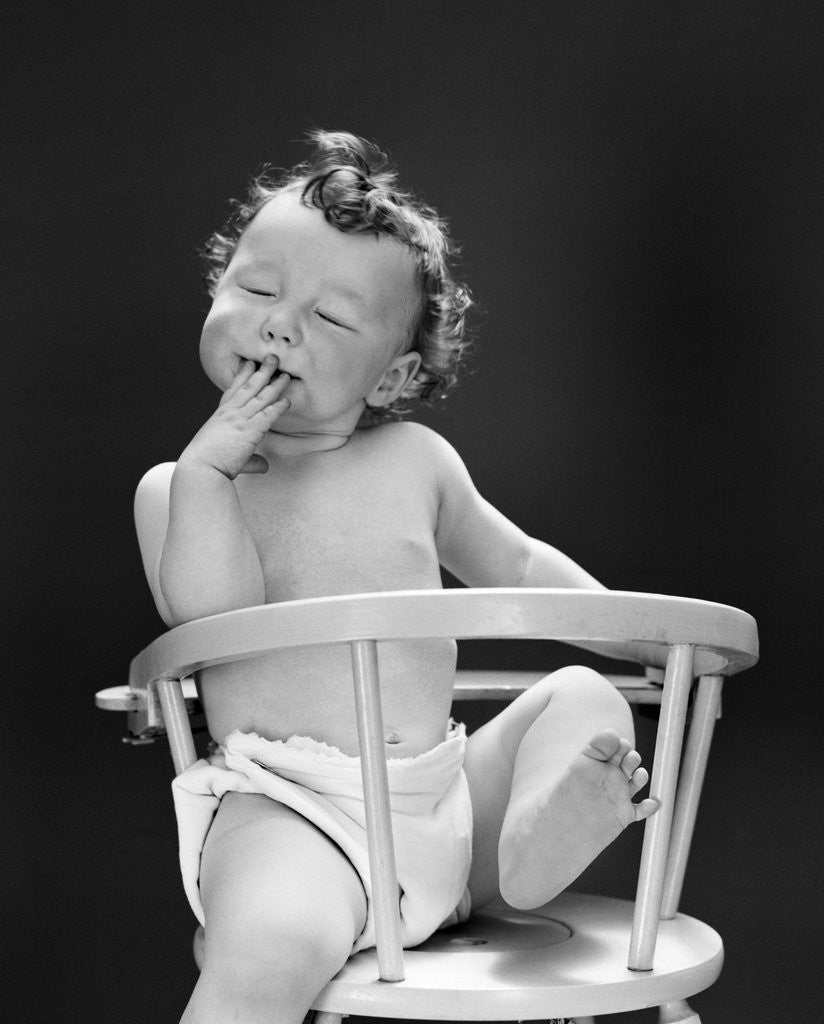 Detail of 1940s 1950s Baby Sitting Backwards In High Chair With One Leg In Air Eyes Closed and Hand On Mouth by Anonymous