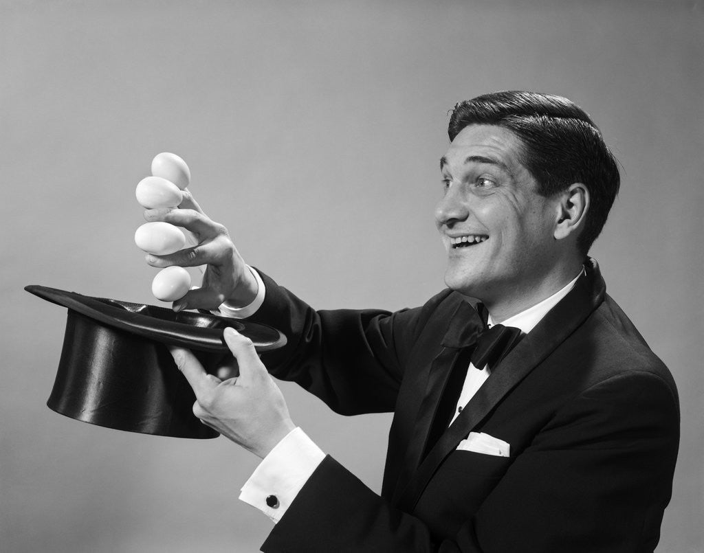 Detail of 1960s Profile Magician Man Pulling 4 Eggs Out Of Hat Holding Them Between Fingers by Corbis