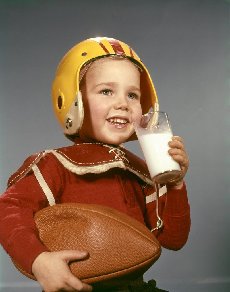 Detail of 1950s 1960s Boy Drinking Glass Milk Wearing Football Helmet Shoulder Pads by Corbis
