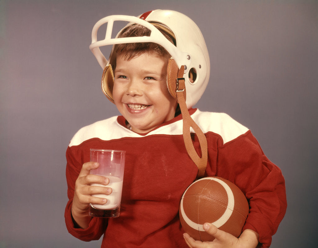 Detail of 1950s 1960s Boy Drinking Milk Wearing Football Helmet Red Jersey Holding Ball by Anonymous