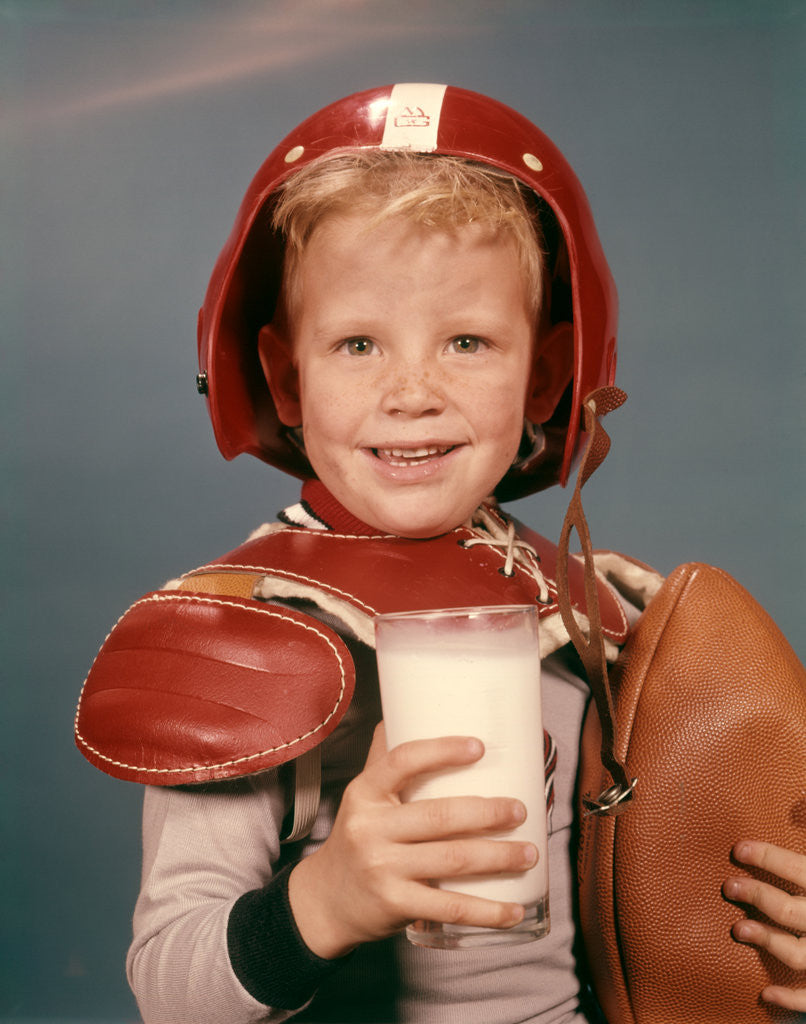 Detail of 1960s Boy Wearing Red Helmet Football Shoulder Pads Holding Glass Milk and Football by Anonymous