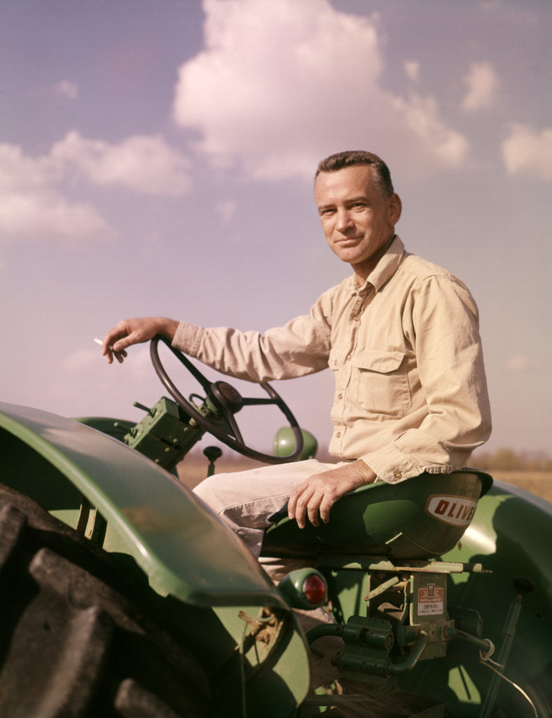 Detail of 1960s Portrait Man Farmer Sitting On Green Tractor Smoking Cigarette by Corbis