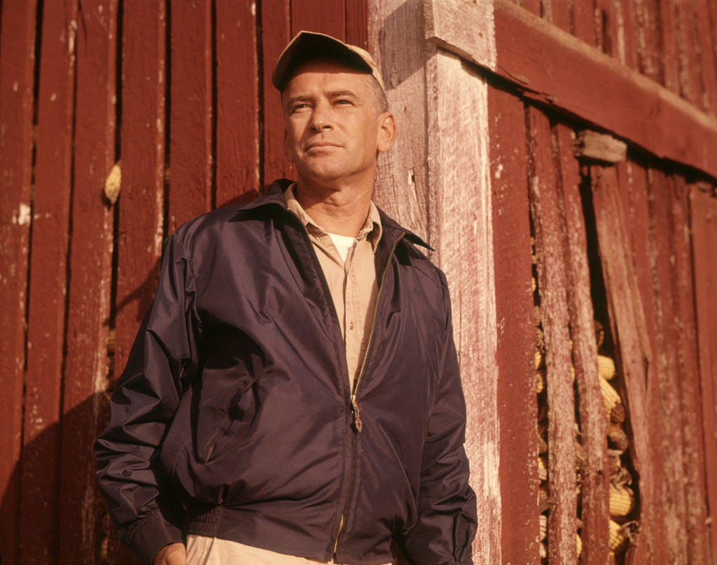 Detail of 1960s Man Farmer Serious Portrait Leaning Against Corn Crib Wearing Cap And Jacket by Anonymous