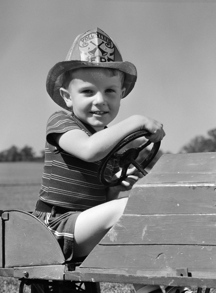 Detail of 1940s Boy Playing Fireman In Toy Fire Truck Wearing Fireman's Safety Hat Holding Steering Wheel by Anonymous