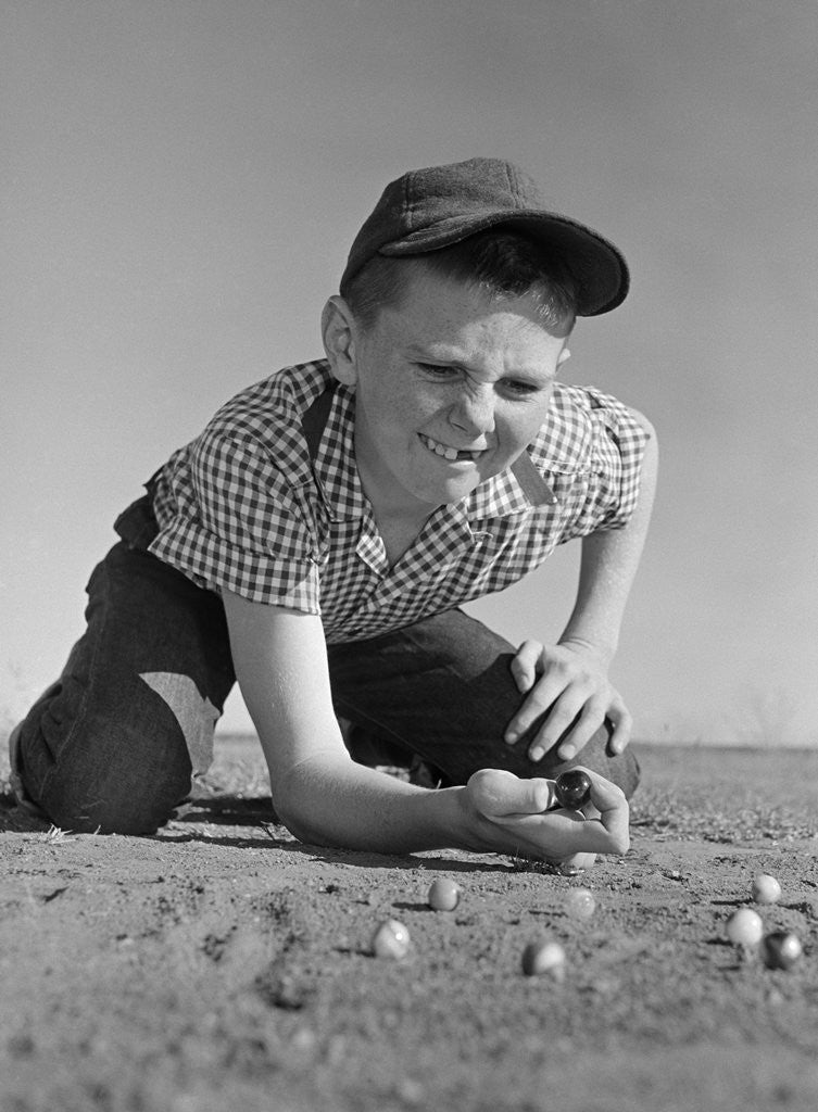 Detail of 1950s 1960s Boy Playing Marbles Kneeling In The Dirt Squinting Missing A Front Tooth by Corbis