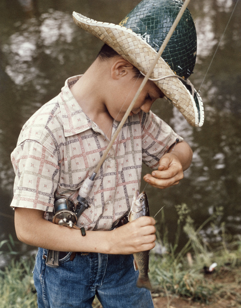 Detail of Boy Wearing Straw Hat Removing Hook From Mouth Of Fish Outdoor by Corbis