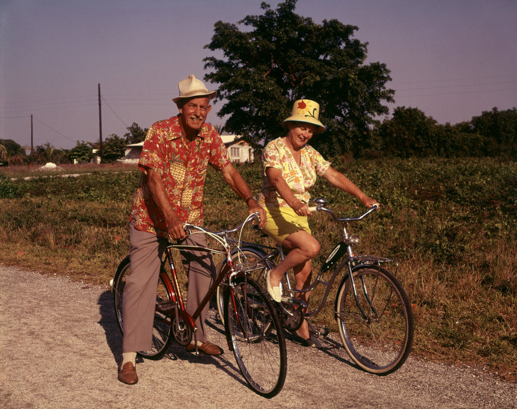 Detail of 1970s Senior Elderly Retired Couple Riding Bikes Wearing Straw Hats Hawaiian Print Shirts by Anonymous