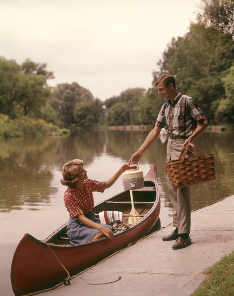 Detail of 1960s Young Couple Loading Picnic Basket Thermos Into Canoe by Anonymous