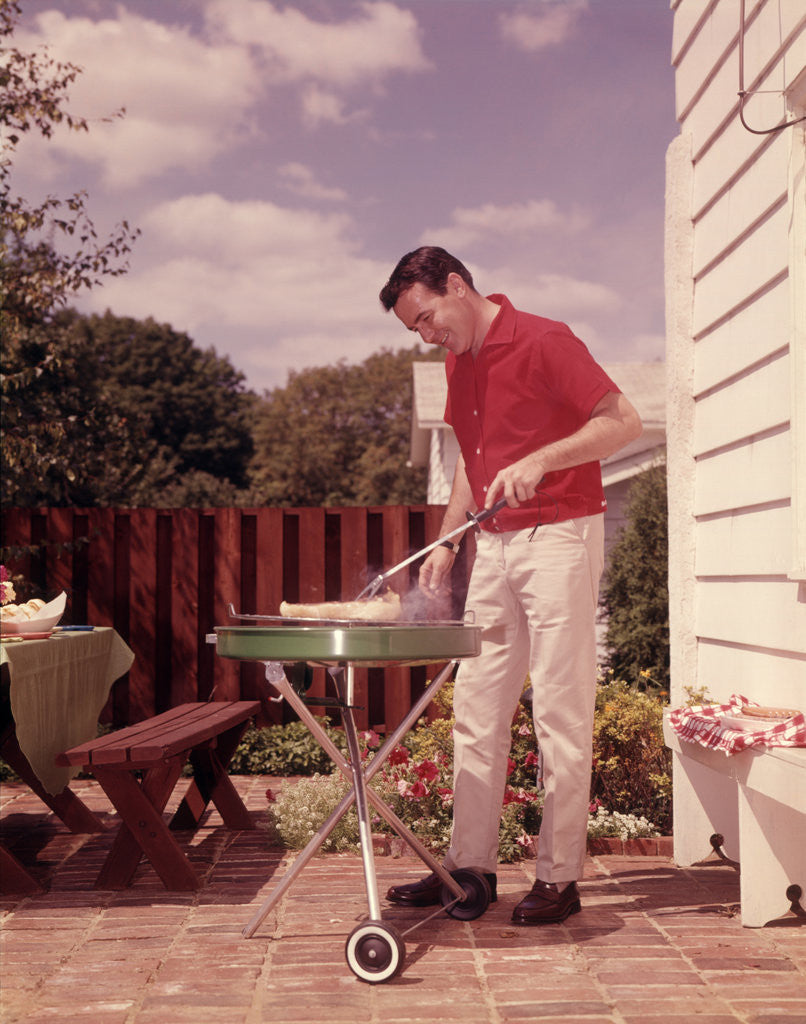 Detail of 1960s Man Wearing Red Shirt Cooking Steak Outdoor On Backyard Grill by Anonymous