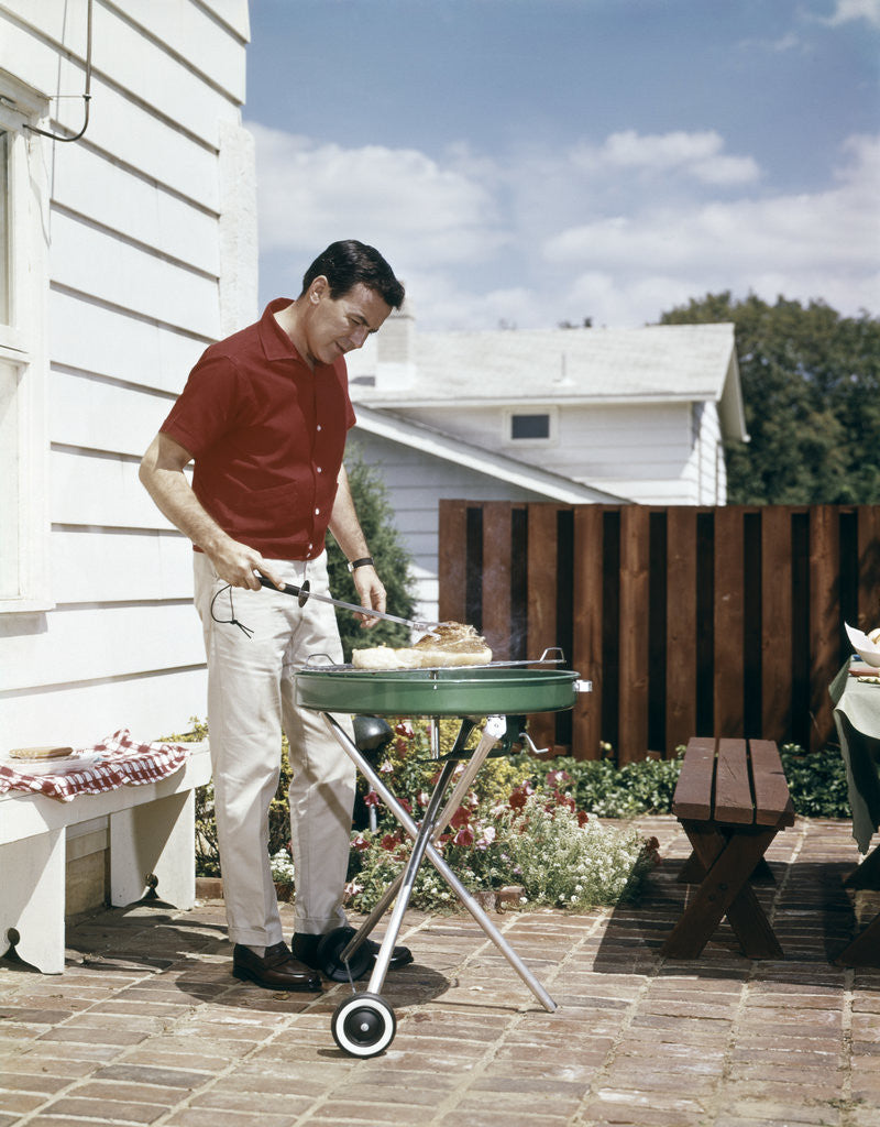 Detail of 1960s Man Wearing Red Shirt Grilling Steak On Backyard Brick Patio by Corbis
