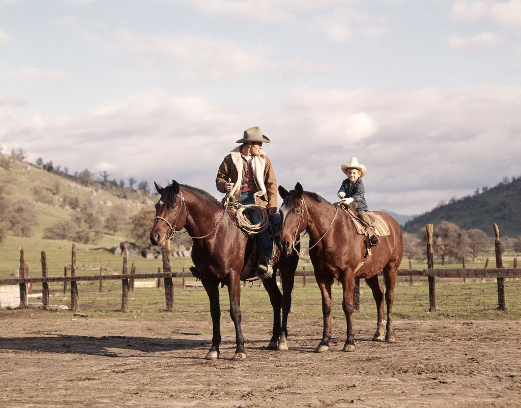 Detail of 1970s Father And Son Sitting Together On Horses By Corral Wearing Hats by Anonymous