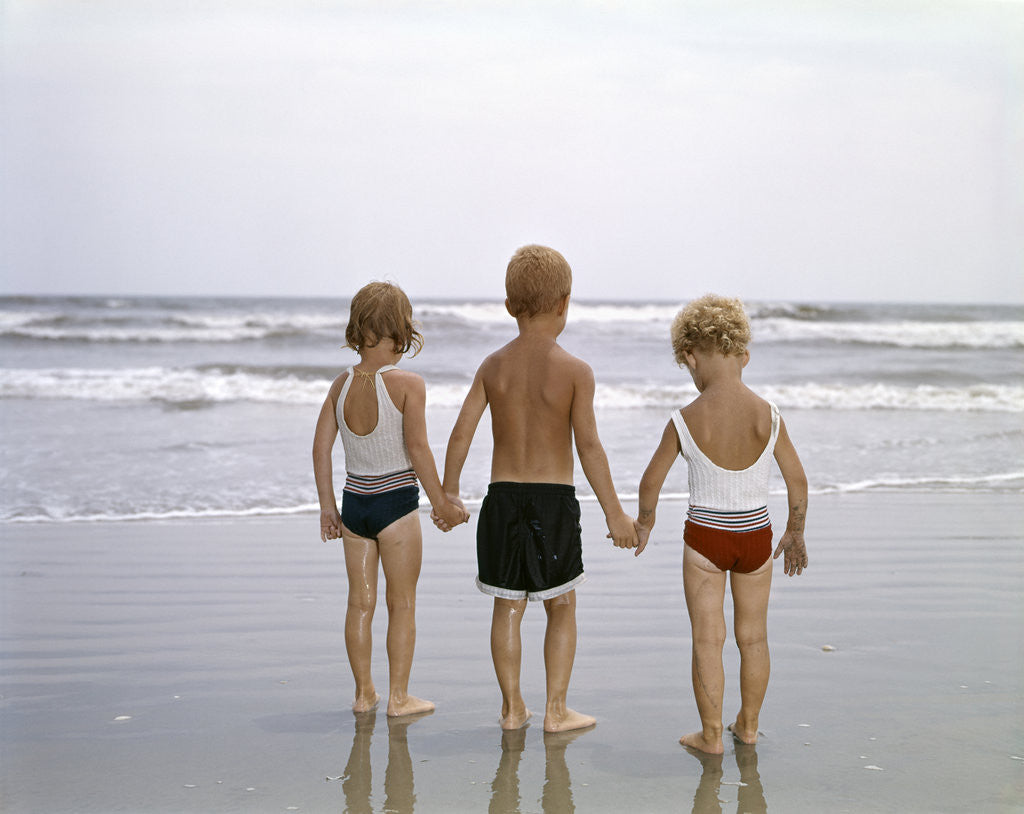 Detail of 1960s Young Children In Bathing Suits Holding Hands On The Beach Looking At The Ocean Waves by Anonymous