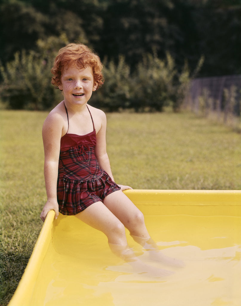 Detail of 1960s Red Haired Little Girl In Plaid Bathing Suit Sitting On Yellow Plastic Backyard Swimming Pool by Anonymous