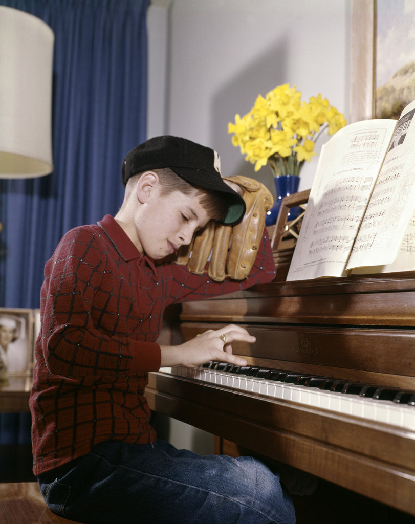 Detail of 1960s 1970s Impatient Annoyed Looking Boy With Baseball Cap And Glove Practicing Piano Lesson by Anonymous