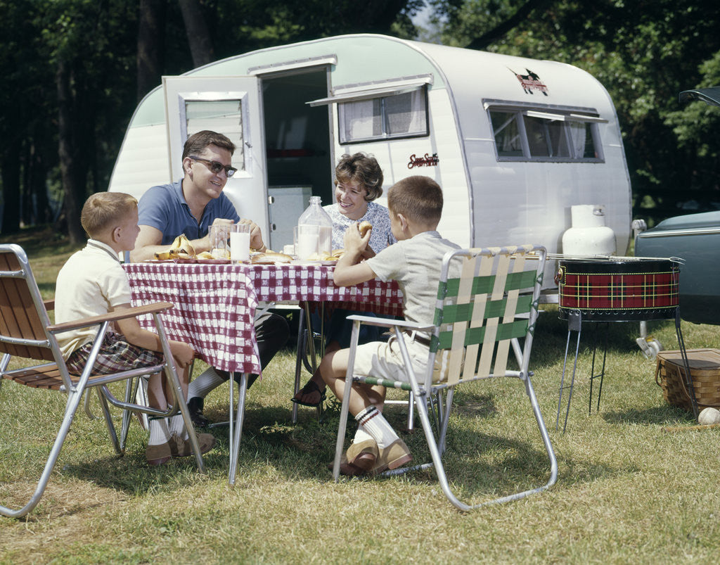 Detail of 1960s Family Sitting In Lawn Chairs At Picnic Table Beside Camping Trailer by Anonymous