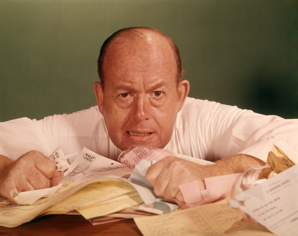 Detail of 1960s Angry Man Businessman Desk Full Of Bills Paper Work Office Stress Frustration by Anonymous