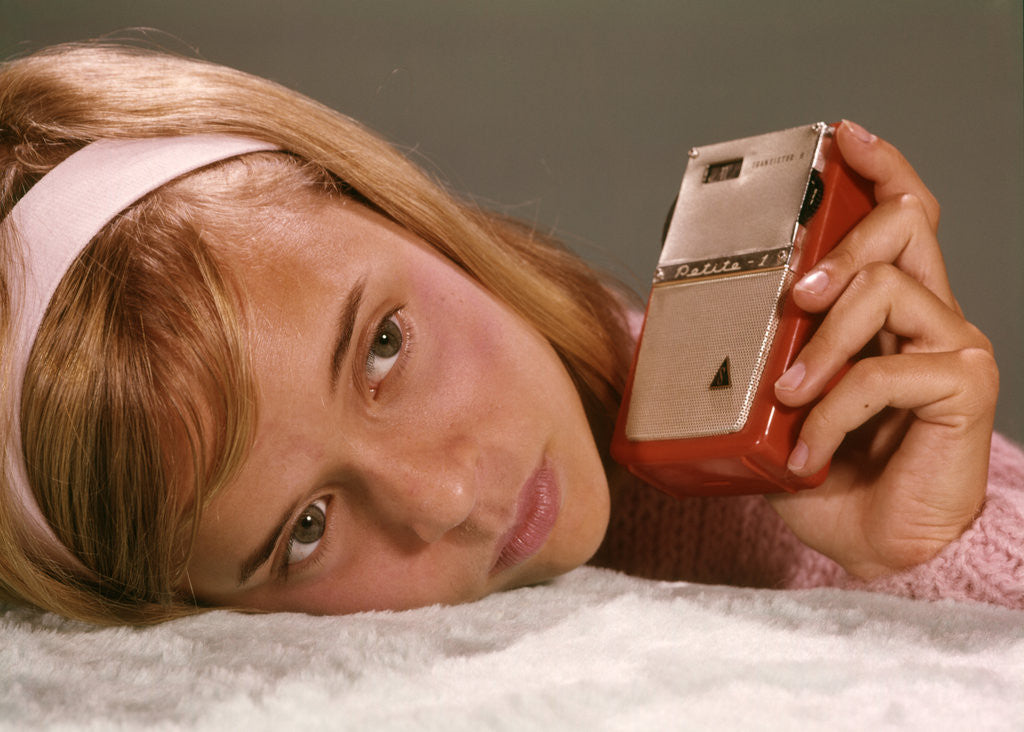 Detail of 1950s 1960s Teenage Girl Holding Red Silver Small Transistor Radio To Her Ear Listening by Anonymous
