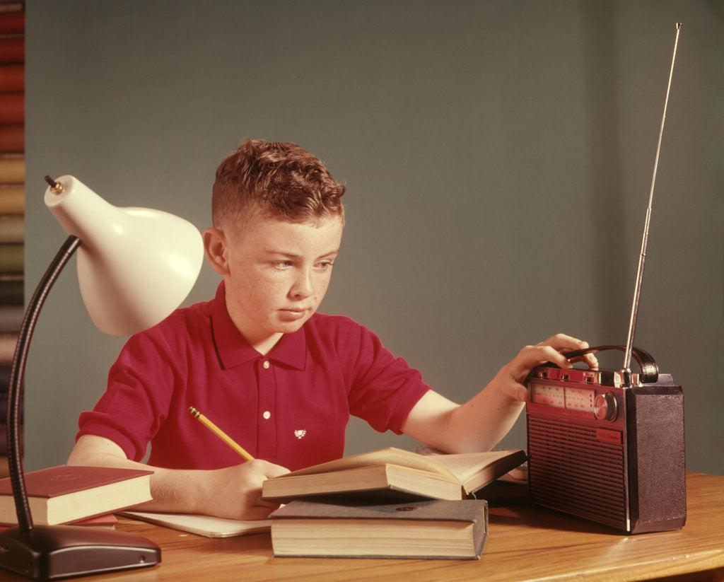 Detail of 1960s Red Hair Boy Sitting At Deslistening To Portable Radio While Studying Homework by Corbis