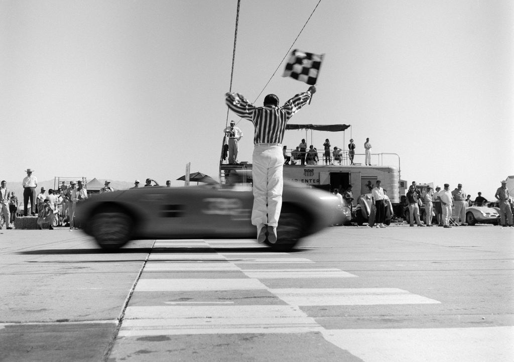 Detail of 1960s Man Jumping Waving Checkered Flag As Winning Sports Car Crossing The Finish Line by Anonymous