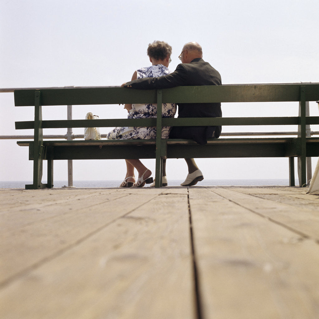 Detail of 1970s Back View Of Senior Couple Sitting On Boardwalk Bench Overlooking Ocean Beach by Anonymous